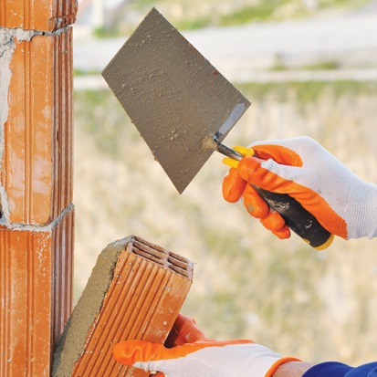 Mala ile tuğla ören koruyucu eldivenli duvar örme ustası