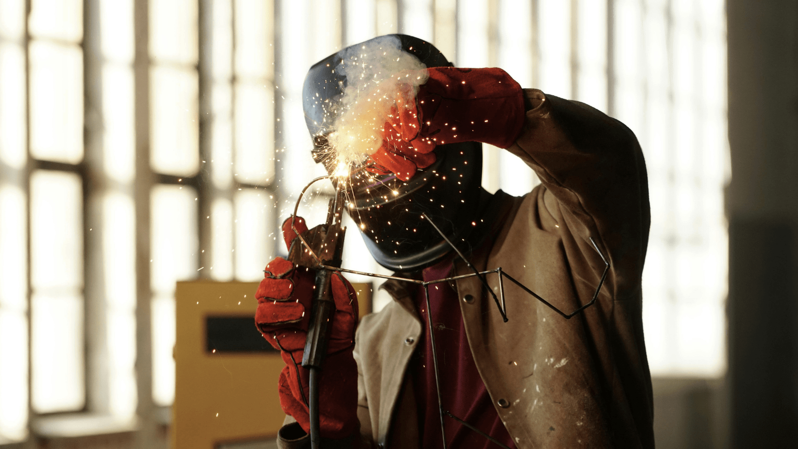 Koruyucu ekipman kullanan otomotiv sac ve gövde işçisi tarafından araç şasi parçaları üzerinde ark kaynağı ile birleştirme işlemi