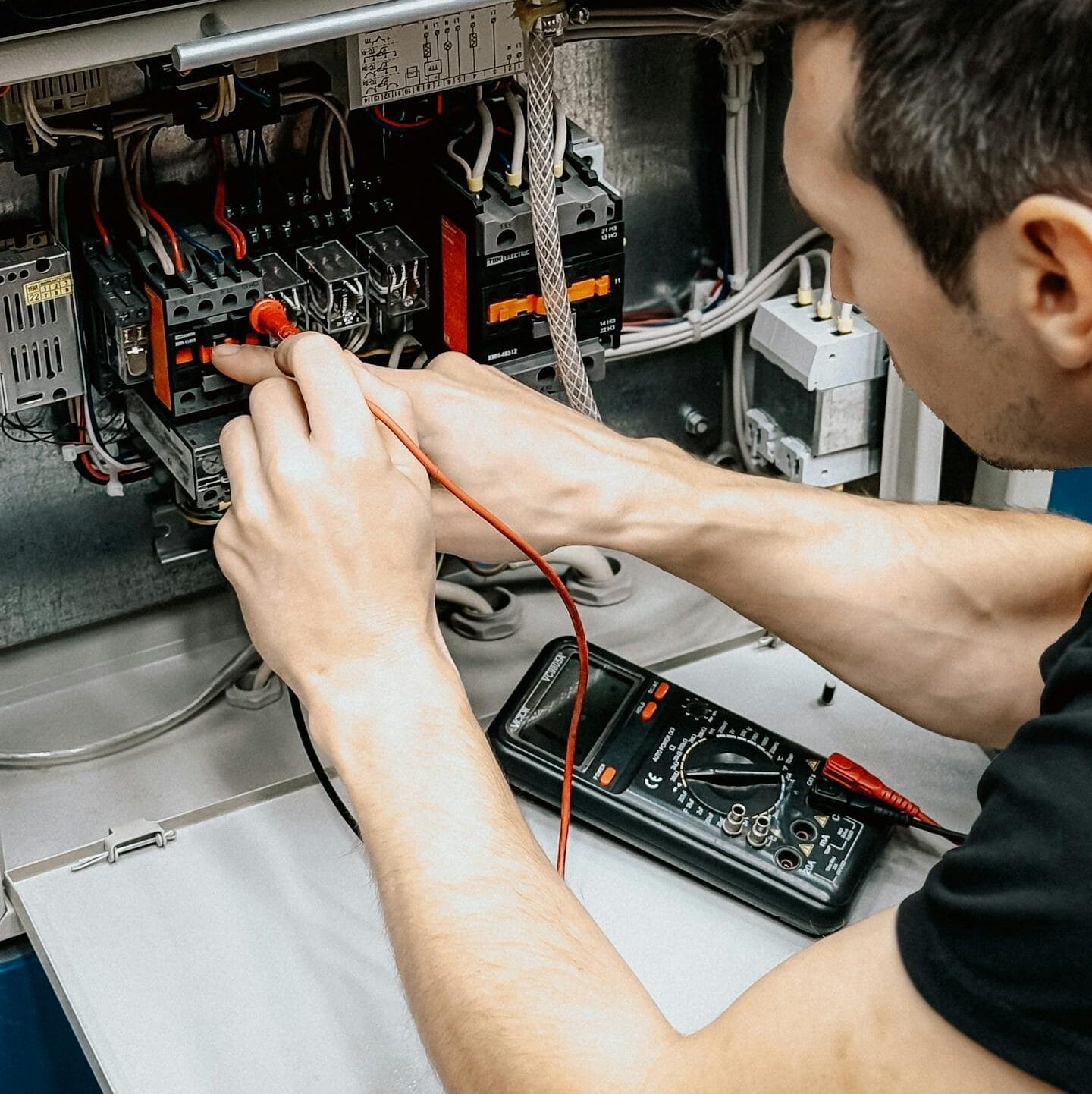 Açık elektrik panosu üzerinde multimetre ile gerilim ölçümü ve devre süreklilik testi yapan teknik uzman